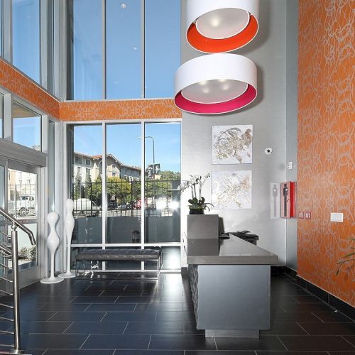 A modern lobby with a reception desk, large windows, orange accents, decorative lighting, artwork on the wall, and a staircase to the left ending the sentence.