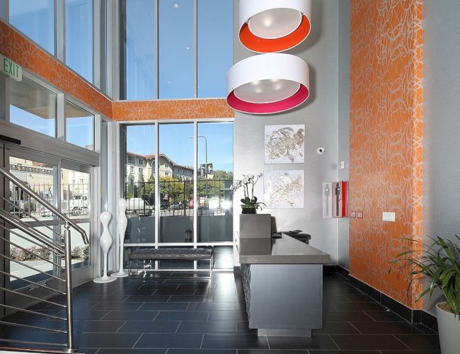 A modern lobby with a reception desk, large windows, orange accents, decorative lighting, artwork on the wall, and a staircase to the left ending the sentence.