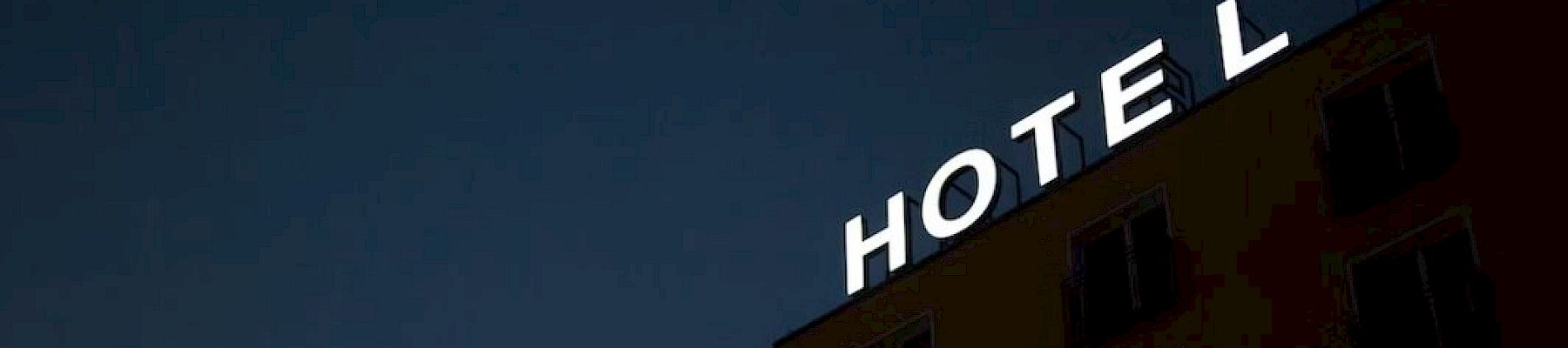 The image shows the side of a building at night with a sign that reads "HOTEL" illuminated in white letters.