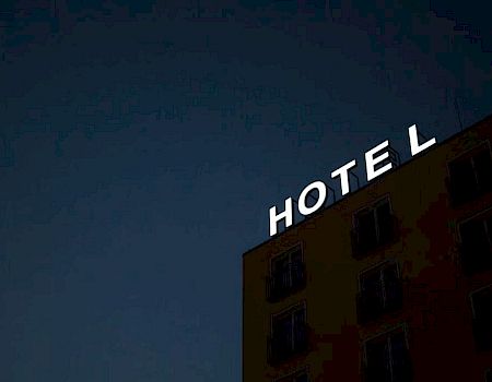 The image shows the side of a building at night with a sign that reads "HOTEL" illuminated in white letters.