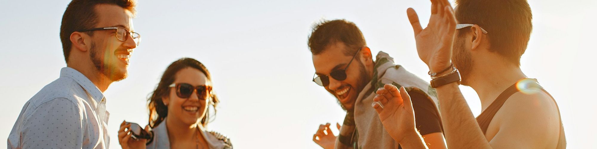 A group of four people are outdoors, laughing and enjoying each other's company in the sunlight.