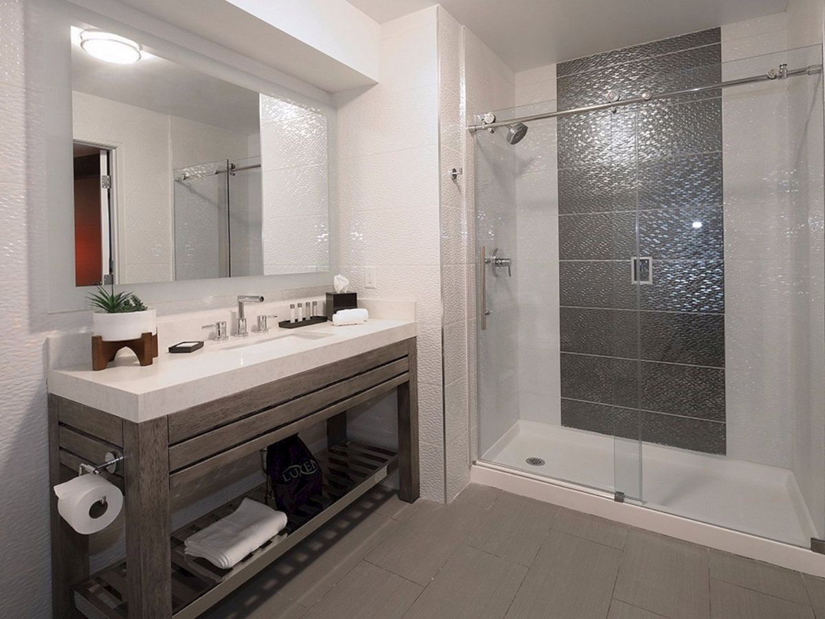 This is a modern bathroom with a large mirror, a sink, a wooden vanity, a walk-in shower with glass doors, and tiled walls and floors.