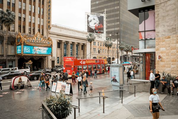 A bustling city street with pedestrians, tour buses, and classic theater marquees, set against a backdrop of tall buildings and busy activity.