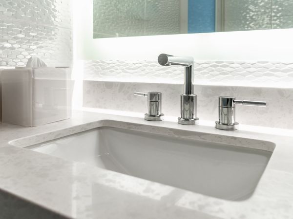 A modern bathroom sink with a marble countertop, featuring a sleek faucet and handles, set in a stylish, brightly lit setting.