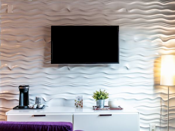A living room with a wavy-patterned wall features a TV, lamp, console, coffee maker, plant, and decorative items.
