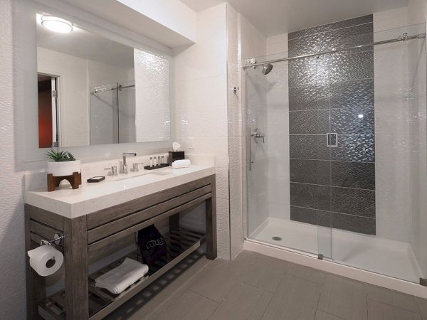 A modern bathroom features a large mirror, a sink with toiletries, a shower with glass doors, and neatly folded towels on a shelf.
