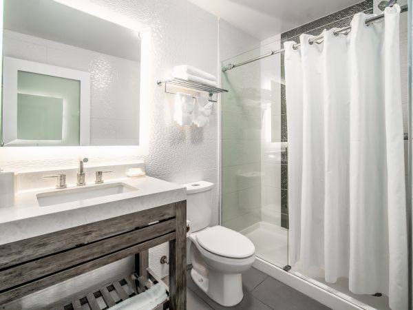 A modern bathroom with a large mirror, sink, toilet, and shower with a curtain in neutral tones.
