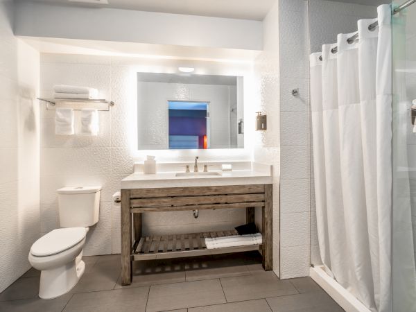 A modern bathroom features a toilet, a wooden vanity with a lit mirror, and a shower with a white curtain.