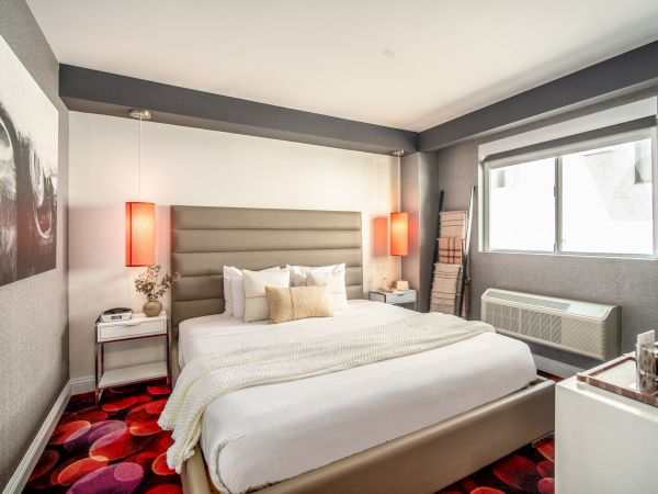 A modern hotel room with a large bed, stylish decor, red carpet, bedside tables, and a window with natural light.