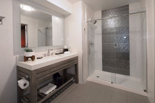 This image shows a modern bathroom with a large mirror above a sink, shelves with towels, and a glass-enclosed shower with gray tiled walls.