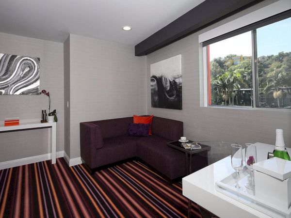 A modern room with striped flooring, artwork, a purple couch, a window with a view, a small table, and a desk holding a wine bottle and glasses.