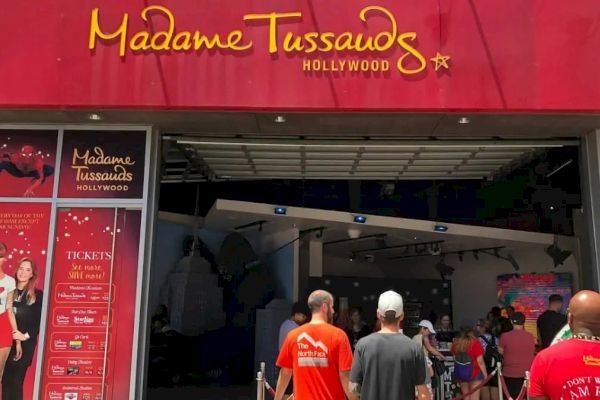 Entrance to Madame Tussauds Hollywood with people in line outside. The entrance has a red sign and posters on either side.