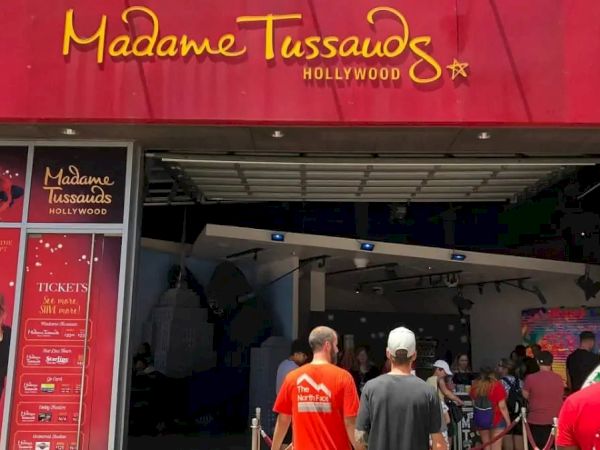 Entrance to Madame Tussauds Hollywood with people in line outside. The entrance has a red sign and posters on either side.