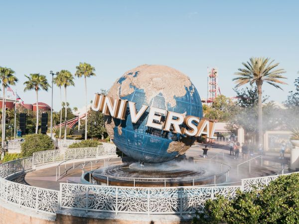 An iconic globe with the word "Universal" is surrounded by palm trees and a fountain, set in a popular theme park.