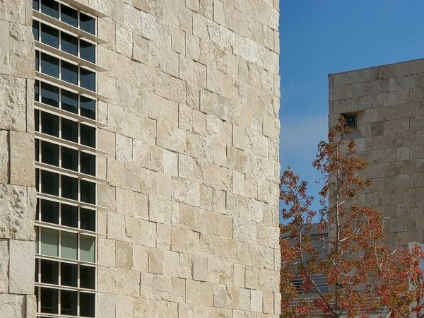 A large stone building with tall windows and autumn trees, with two people walking along the pathway in front of it.