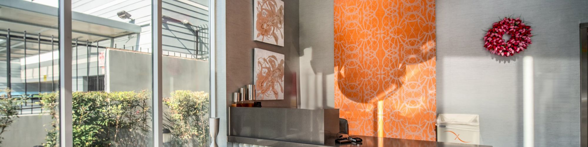 A modern lobby features a textured reception desk, colorful artwork, and large pendant lights, with natural light streaming through windows.