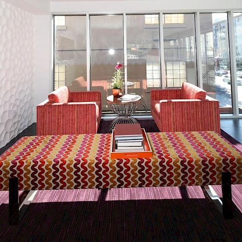 A modern lounge with red-patterned furniture, a geometric bench, books on a tray, a potted plant, and a TV on a textured white wall ending the sentence.