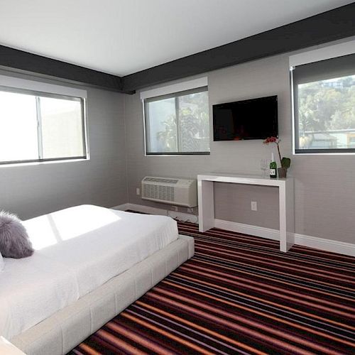 A modern bedroom with a large bed, striped carpet, two windows, a wall-mounted TV, and a small desk with decorative items ending the sentence.