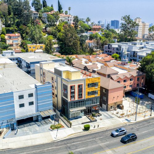 The image shows a street with buildings on a hillside, various cars on the road, and greenery in the background.