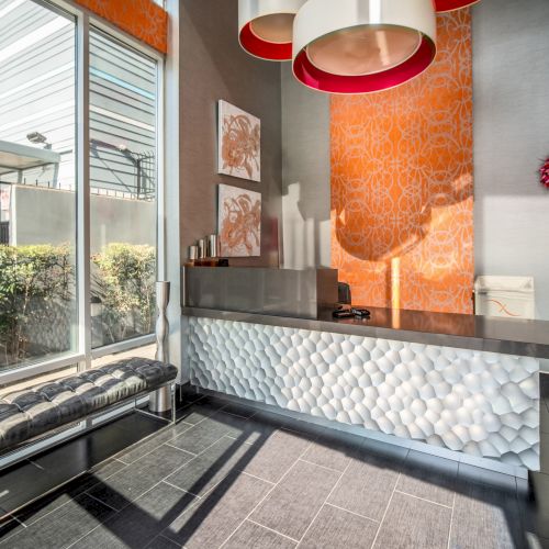 The image shows a modern reception area with a stylish desk, wall art, large windows, and decorative lighting, creating a welcoming atmosphere.