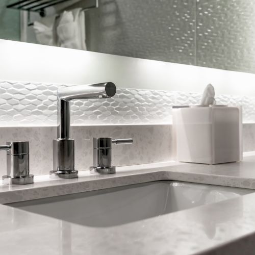 A modern bathroom sink with a sleek faucet, accompanied by a white tissue box and a large mirror with ambient lighting.