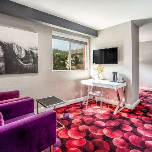 A modern room with purple sofas, vibrant red-patterned carpet, abstract art, a TV, and a scenic window view.