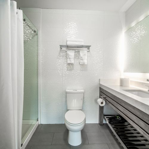 A modern bathroom with a shower, toilet, and sink. The walls and fixtures are sleek and minimalistic, creating a clean, bright atmosphere.