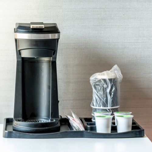 A single-serve coffee maker with coffee pods and disposable cups is neatly arranged on a tray on a countertop.
