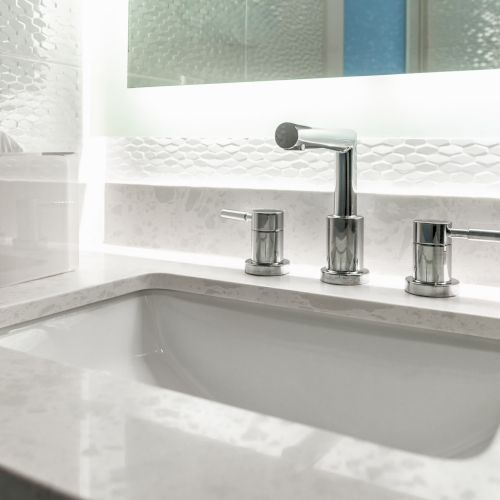 A modern bathroom sink with a marble countertop and chrome faucet, set against a textured wall and a mirror in the background.